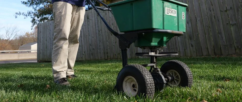 Crew in Wilmington Manor, DE, pushing a fertilizer spreader across a lawn.