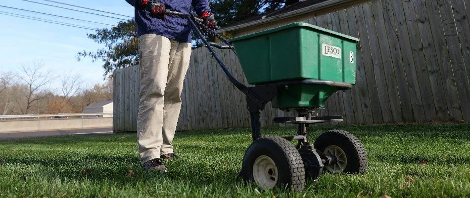 Tech pushing a granular spreader across a lawn in Claymont, DE.