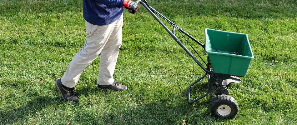 Worker pushing a seed spreader across a lawn in Newtown Grant, PA.