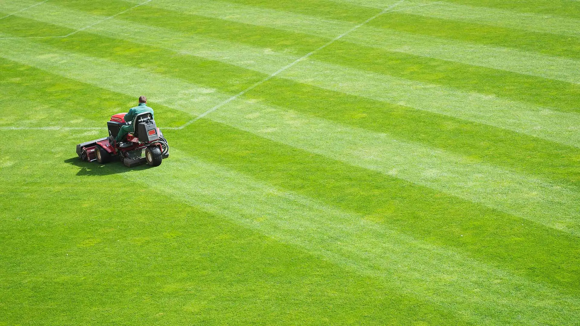A man is aerating an athletic field with a large, riding aerator.
